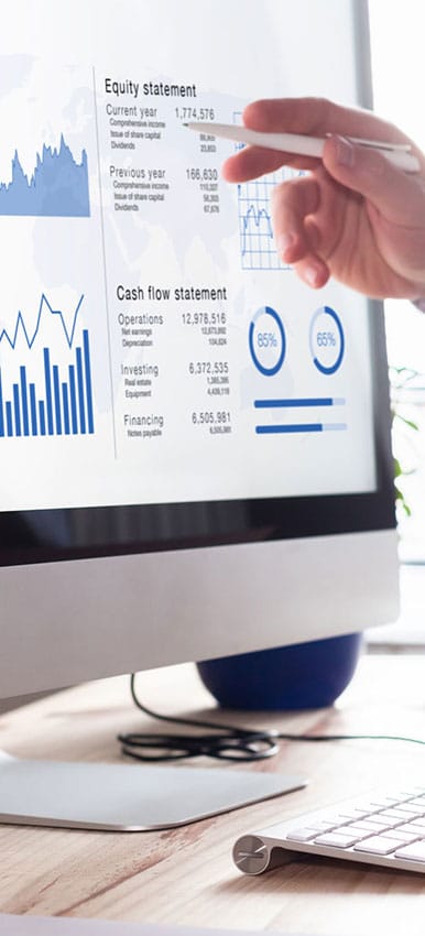 Person using a stylus to point at a computer monitor showing financial charts and a cash flow statement on a desk.